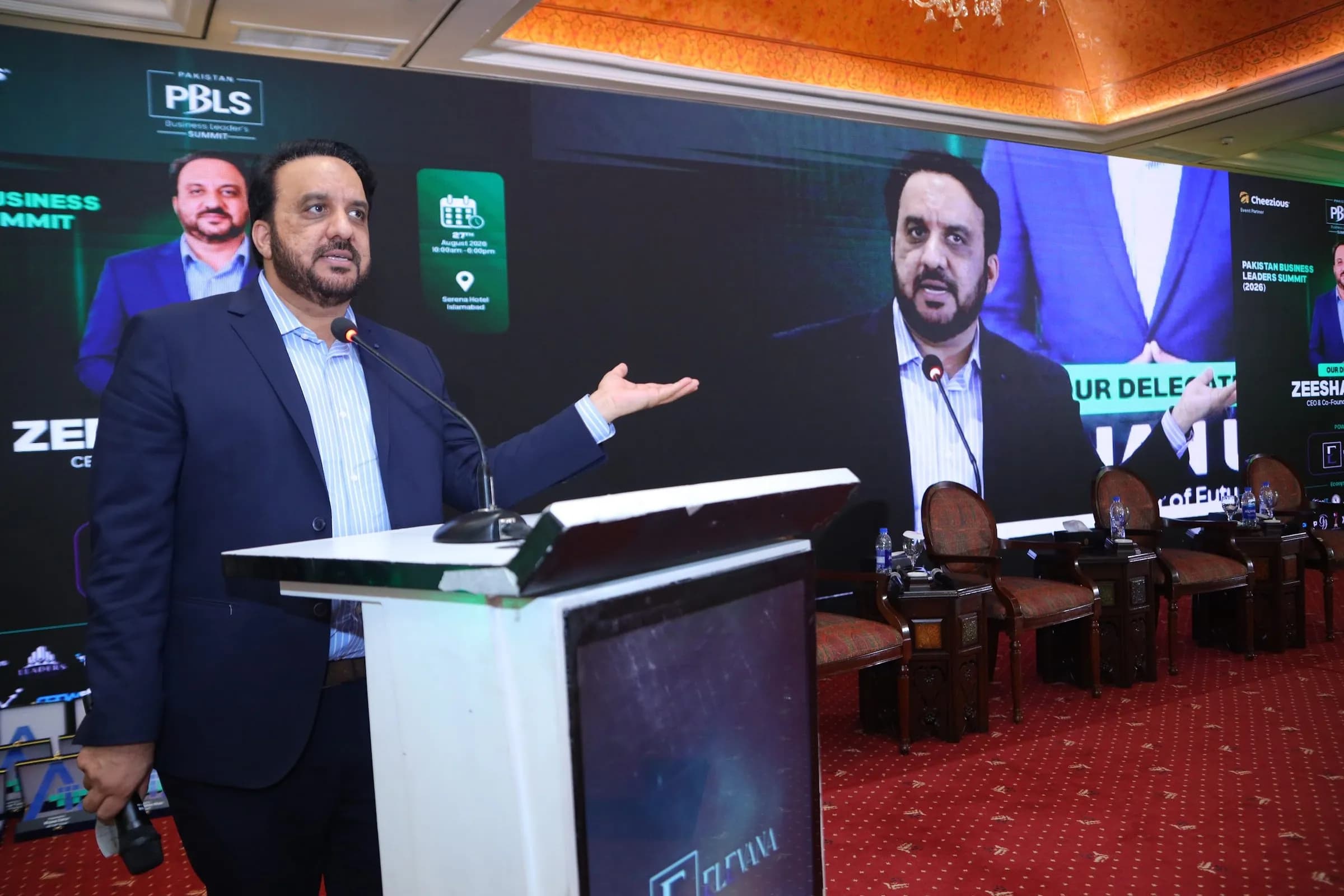 A speaker at the podium gesturing towards the screen at PBLS Serena Islamabad
